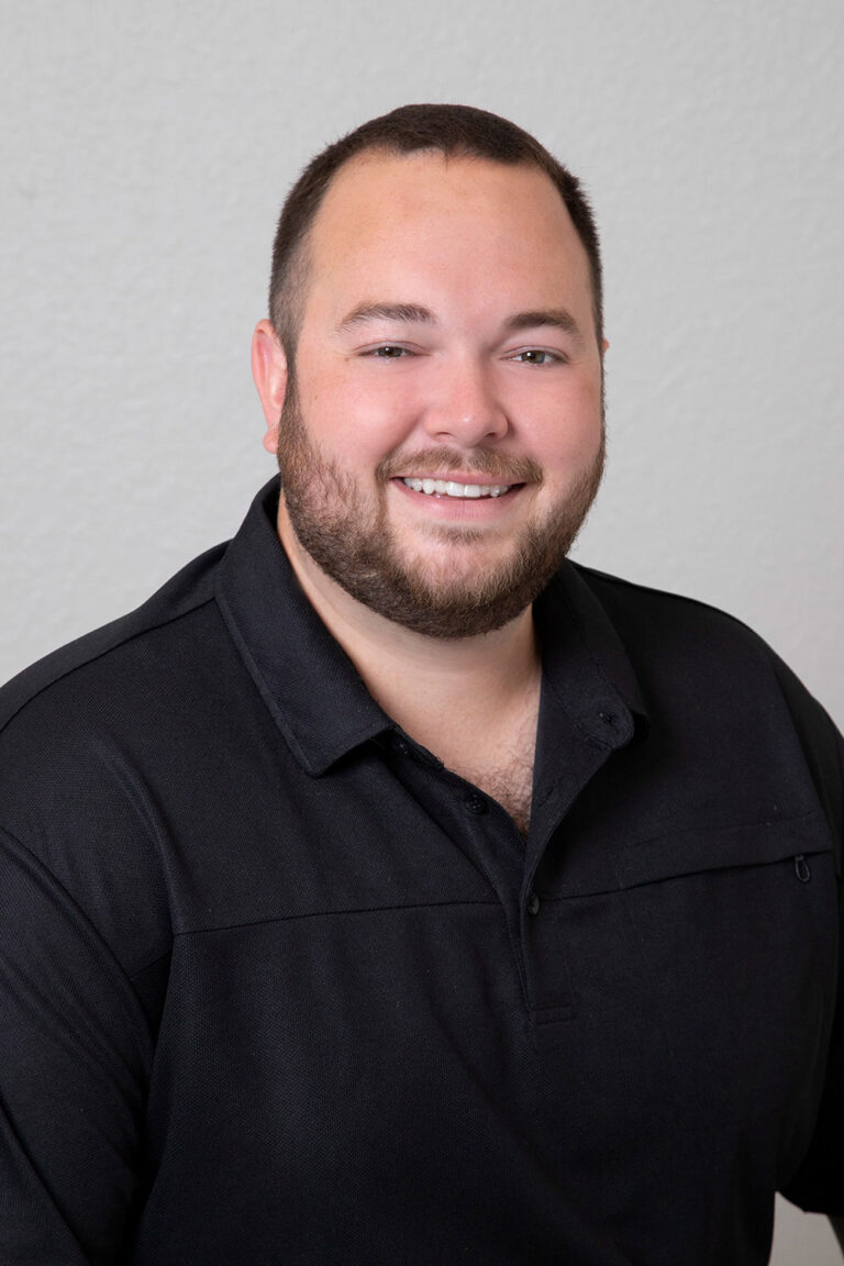 Headshot for Ross Glo Dental Studio's Receptionist in a black collared shirt is set against a plain, light-colored background. He faces the camera with a calm, confident expression, presenting a clean and professional look.