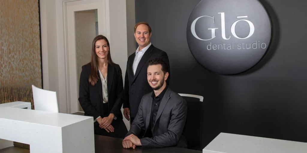 Dr. Andrea Emmerich, Dr. Jake Jacomet, and Dr. Nicholas Dwan sitting at the front desk of Glo Dental Studio in Waukesha, WI.